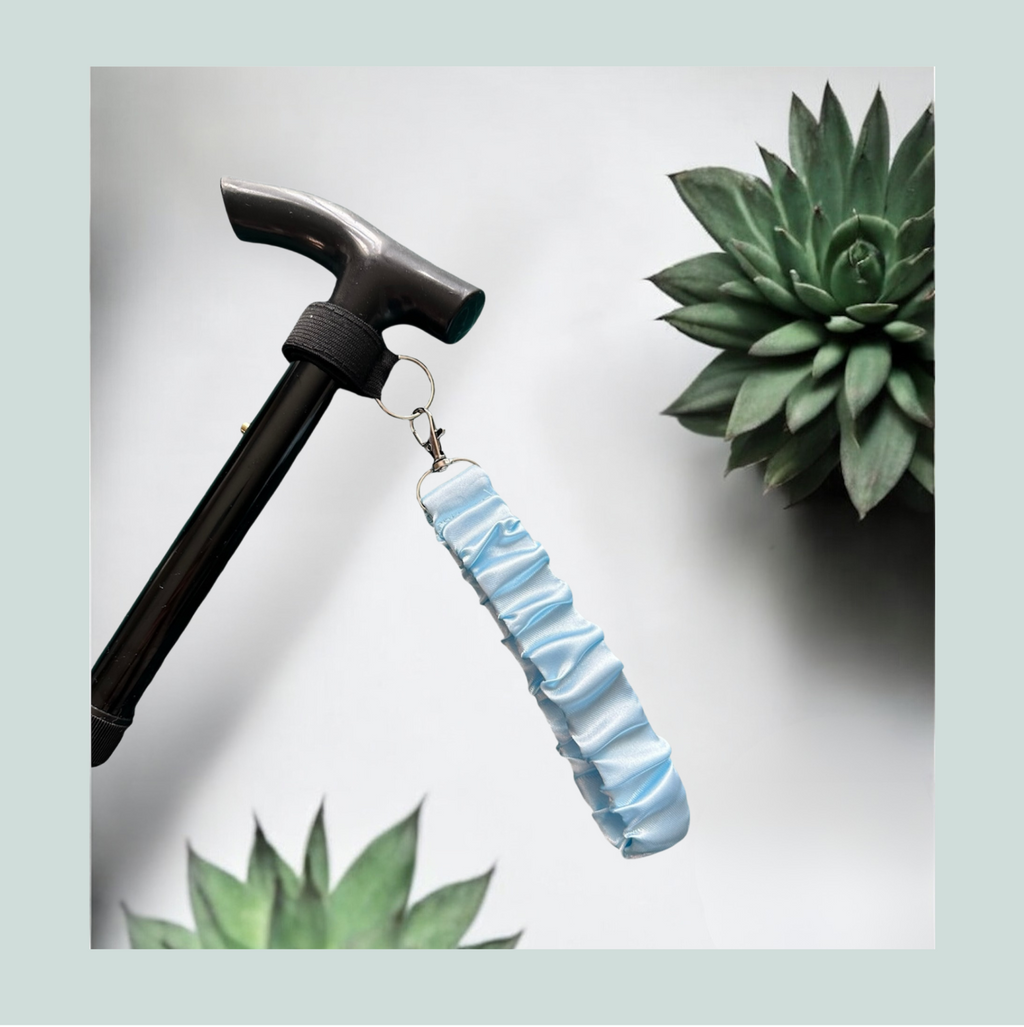 A light blue ruched wrist strap attached to a black cane, displayed against a white background with decorative succulent plants.