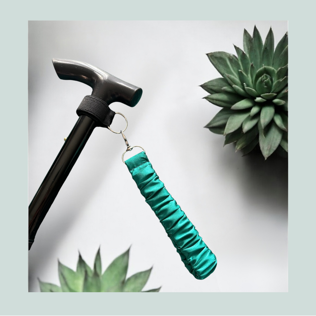 A close-up product shot of a black hammer handle with a bright teal green fabric grip cover attached by a small metal ring. The scene is styled with succulent plants against a light gray background