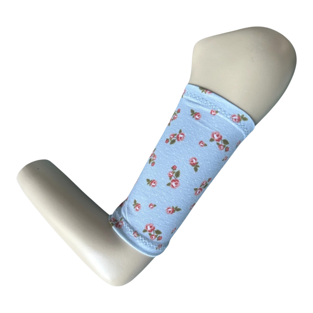 Pale blue picc line fover with a rose print in red and white with green leaves. Armband is displayed on a maneqinn arm.