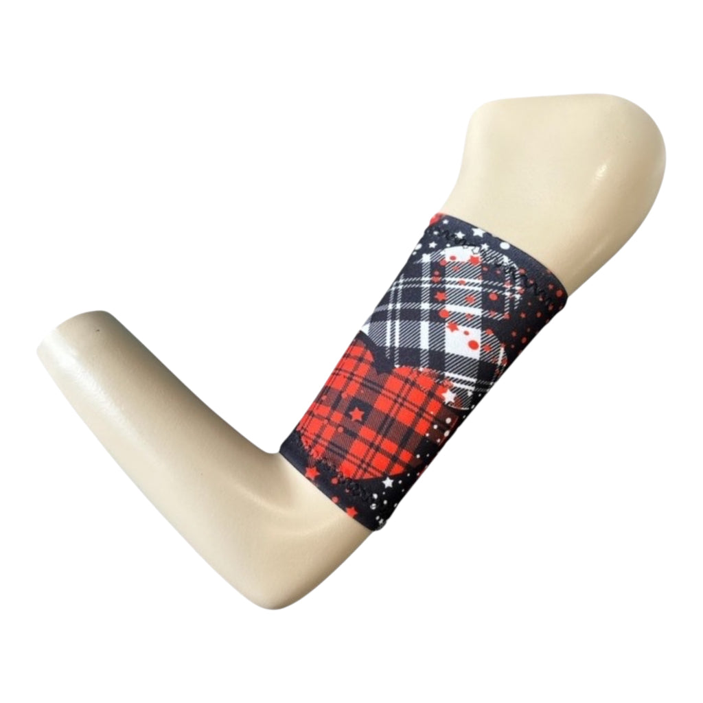 A tartan theme print picc line cover displyed on a mannequinn arm. The armband has a black background with larger hearts in tartan print. One heart is red and blak tartan, the other white and black. With red and white tiny stars sprinkled on the design.